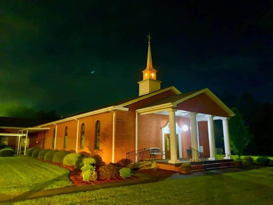 Pleasant Grove Baptist Church building lit up at night, with its white steeple and columned front porch