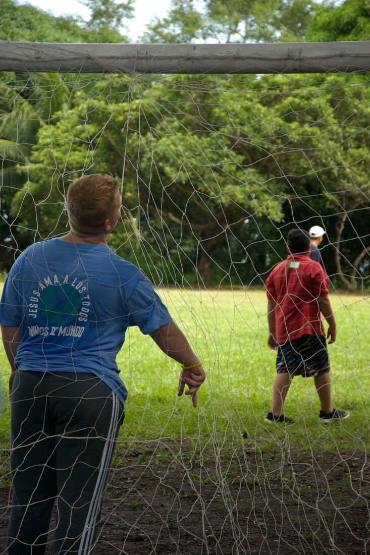 A Pleasant Grove team member playing soccer with children on a grass field in El Salvador