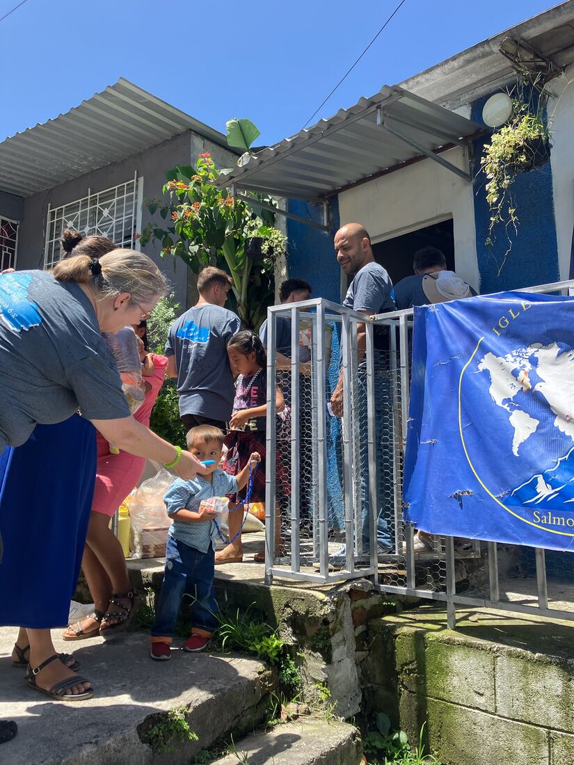 Team members handing out supplies to children beside a church banner in El Salvador