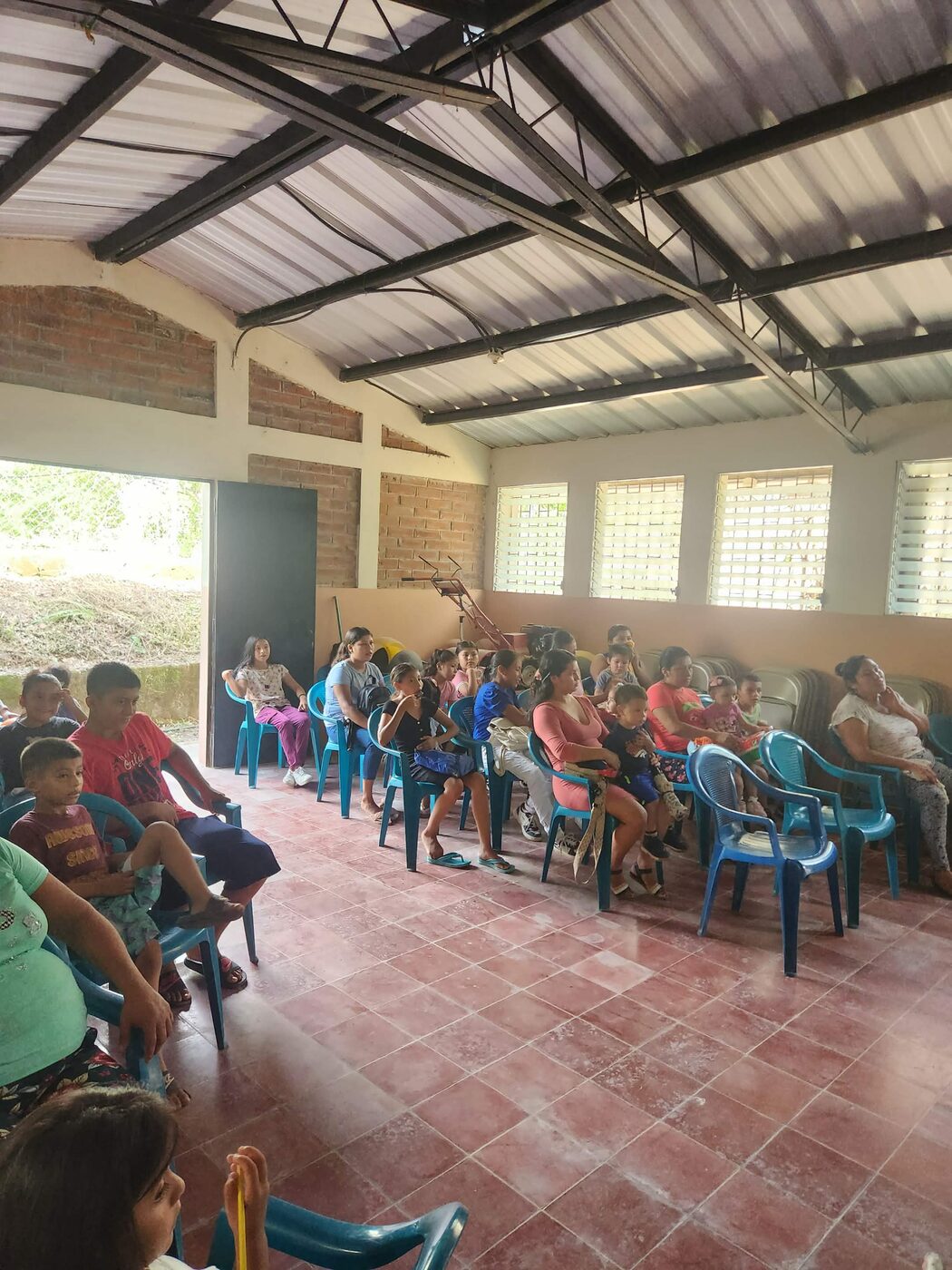 A wide view of children and volunteers gathered under a covered pavilion in El Salvador for a shoebox distribution