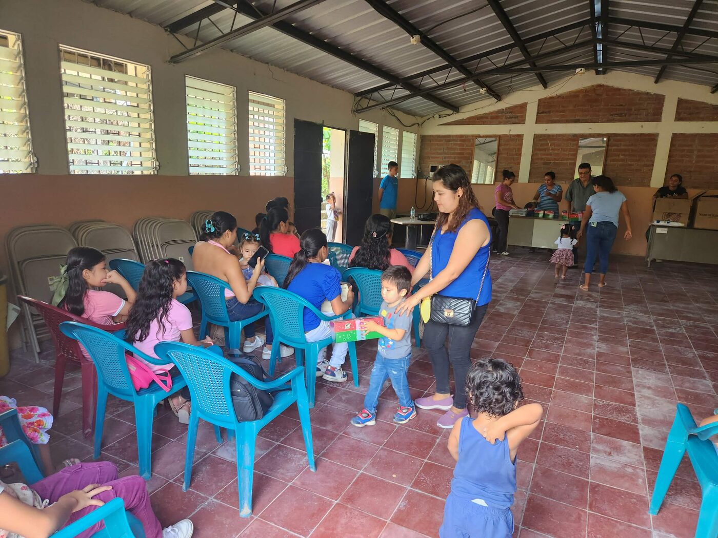 A volunteer hands an Operation Christmas Child shoebox gift to a young boy inside an open-air church pavilion in El Salvador